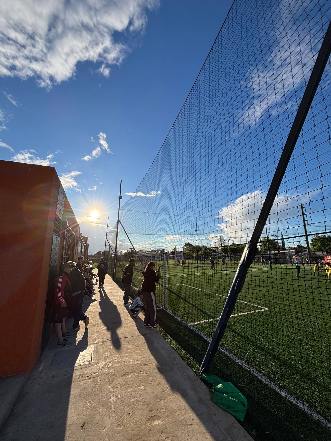 Padres mirando un partido al costado de la cancha de L10, al atardecer