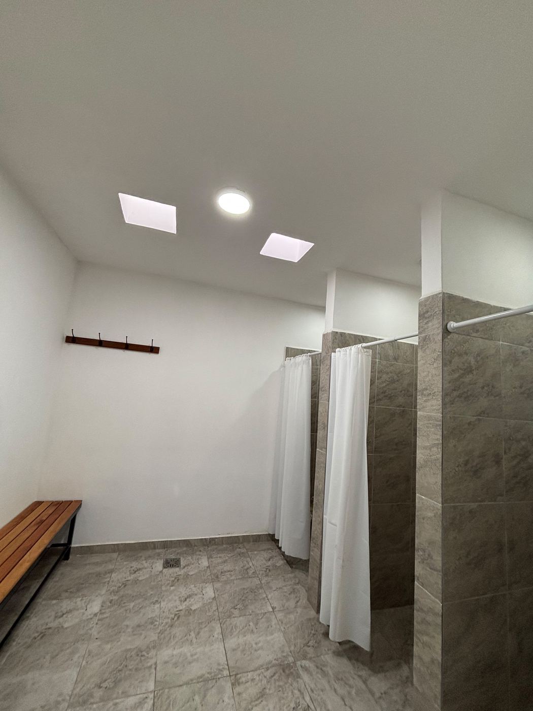 Vestuario con duchas, banco de madera y perchero